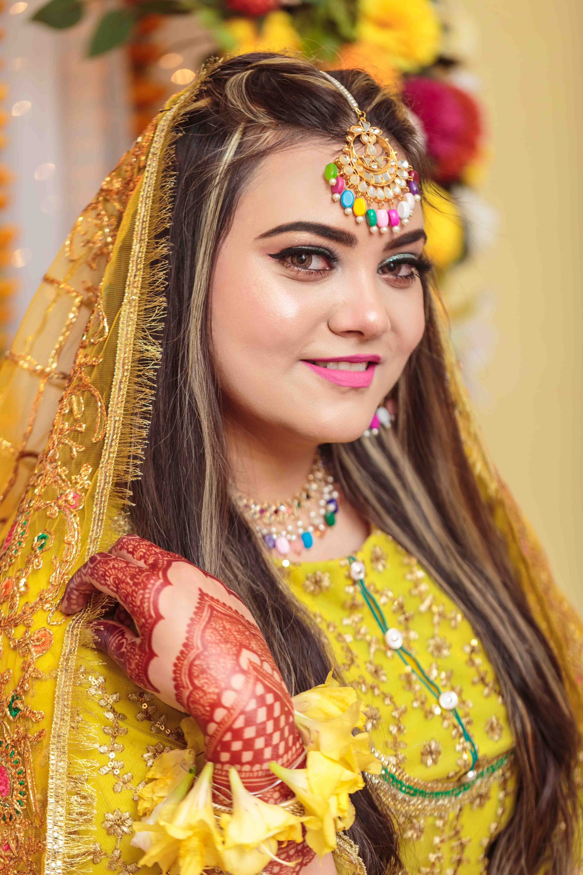 Woman in traditional yellow bridal outfit with jewelry and flowers, smiling.