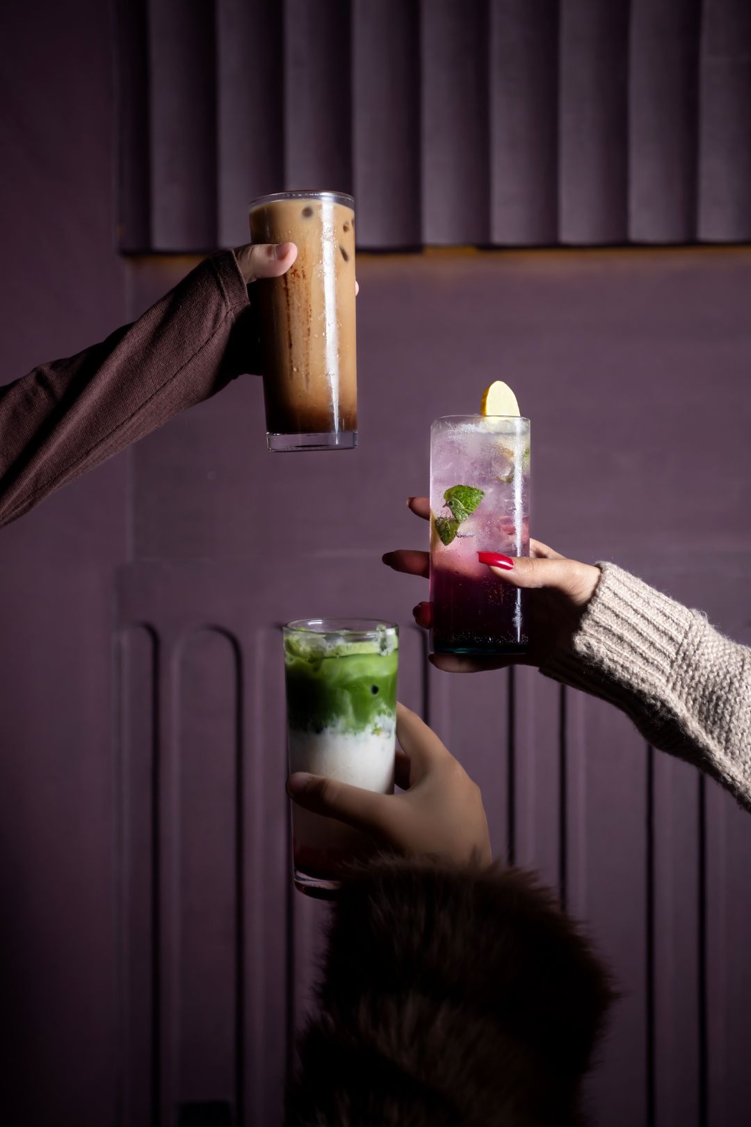 Three hands holding glasses with drinks against a purple background