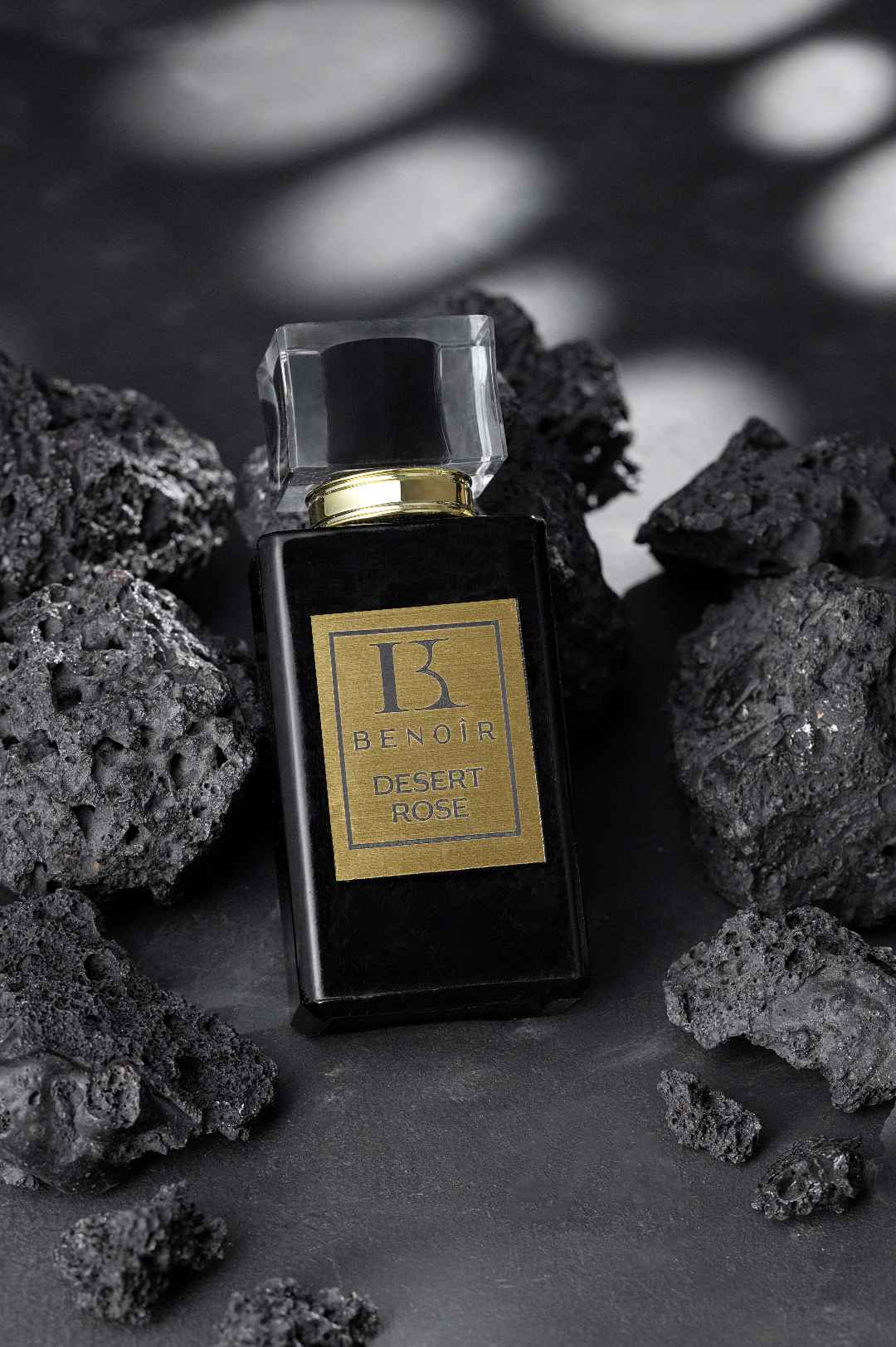 creative studio photography of a black perfume bottle surrounded by rough black stones